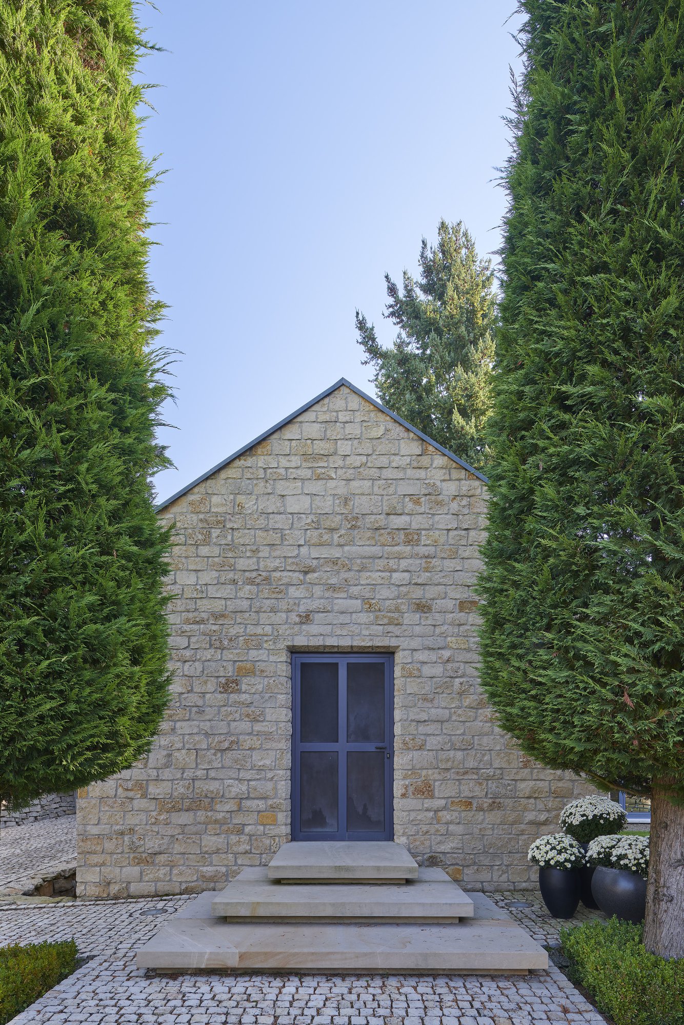 Architekturfotografie Haus S., Bliesgau — Giebelseite aus Kalkstein mit Eingangstür zwischen hohen Hecken