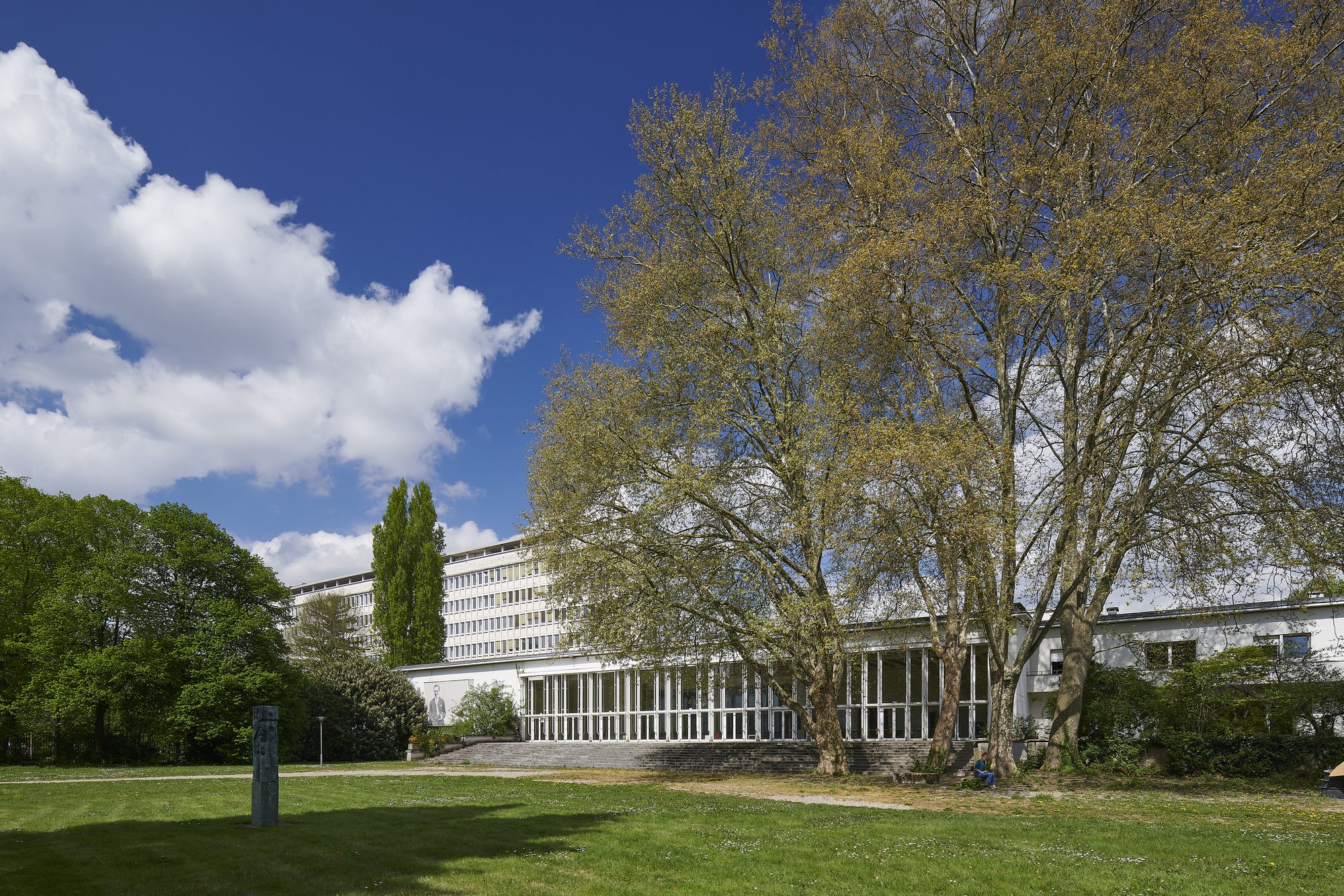 Architekturfotografie ehemalige Französische Botschaft, Saarbrücken — Blick über den Park auf den verglasten Flachbau, dahinter das Bürohochhaus