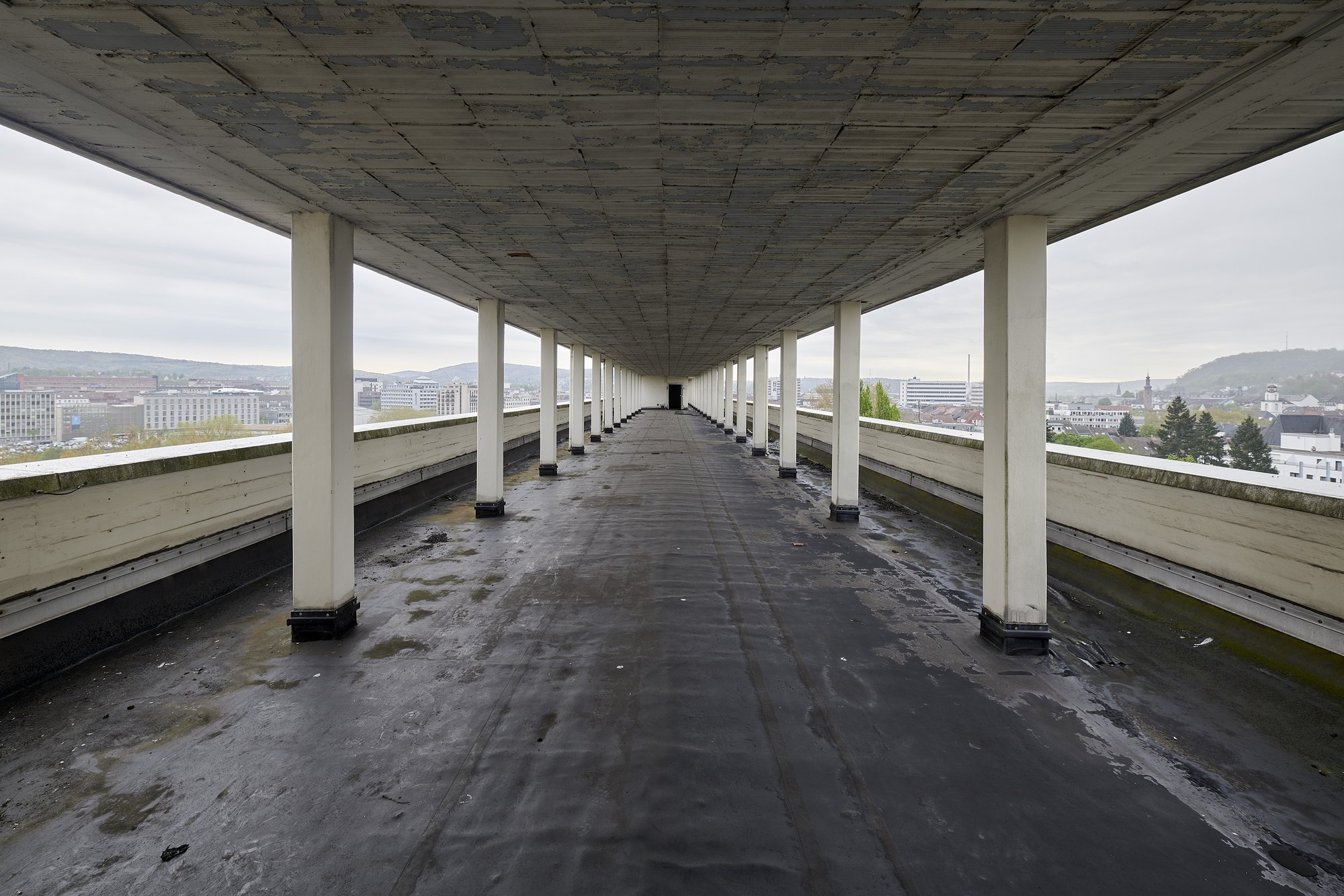 Architekturfotografie ehemalige Französische Botschaft, Saarbrücken — Stützenreihe auf der Dachterrasse, dahinter der Stadtrand